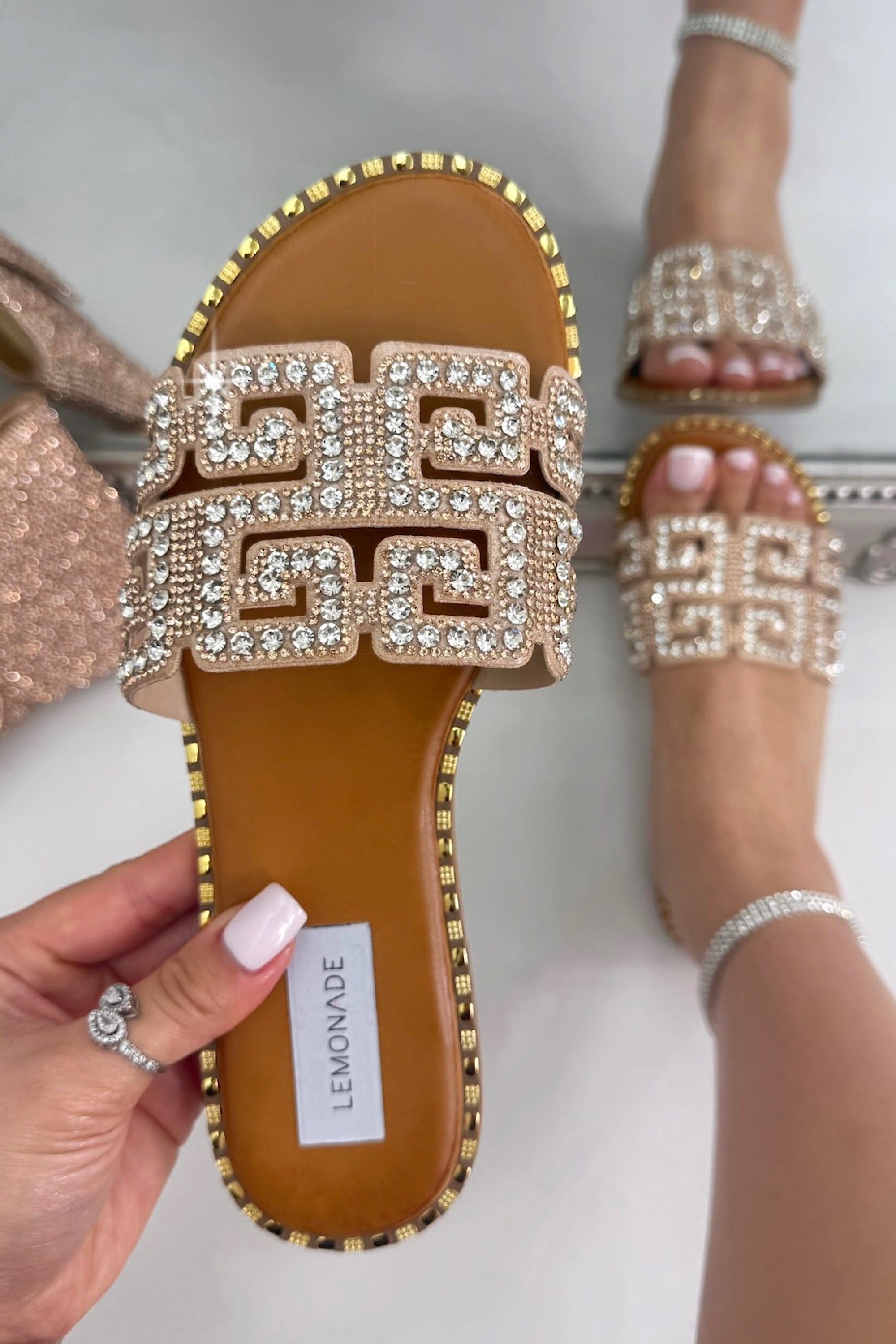 Decorative sandal with embellishments held by a hand, brand &