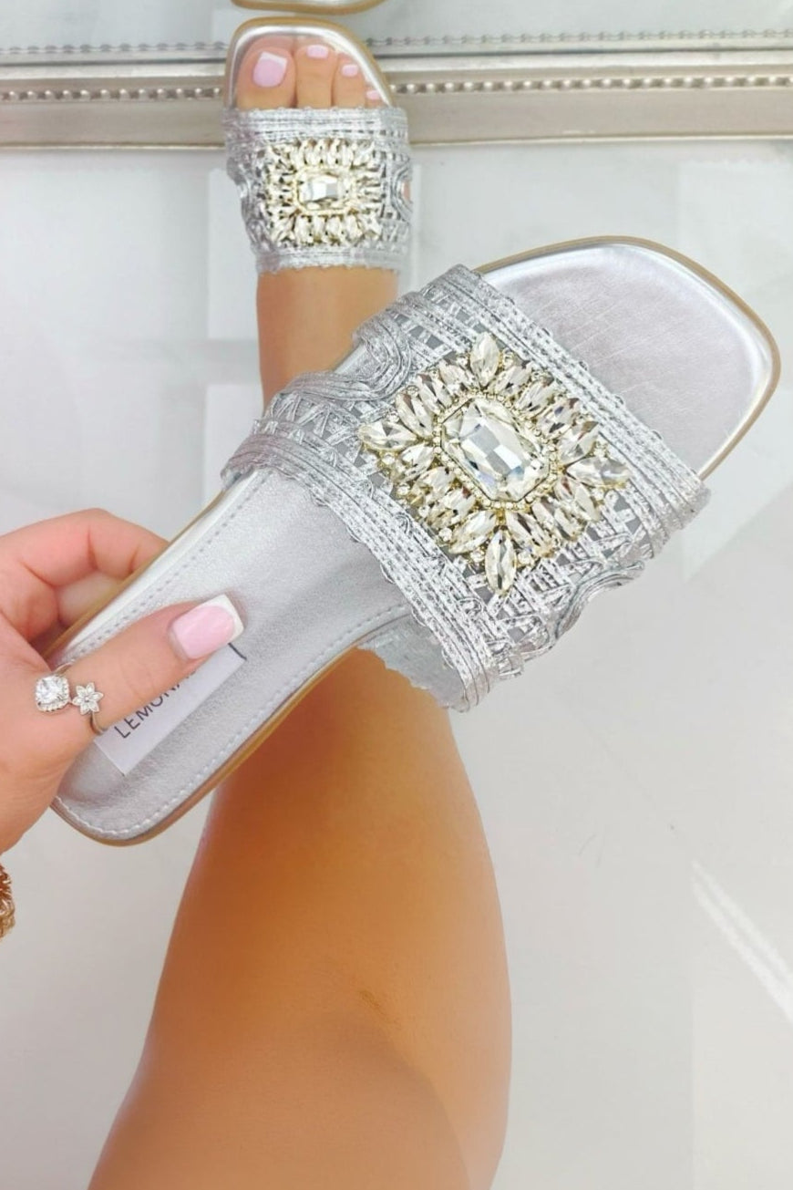 Silver flat shoes with clear soles held by a hand against a white background