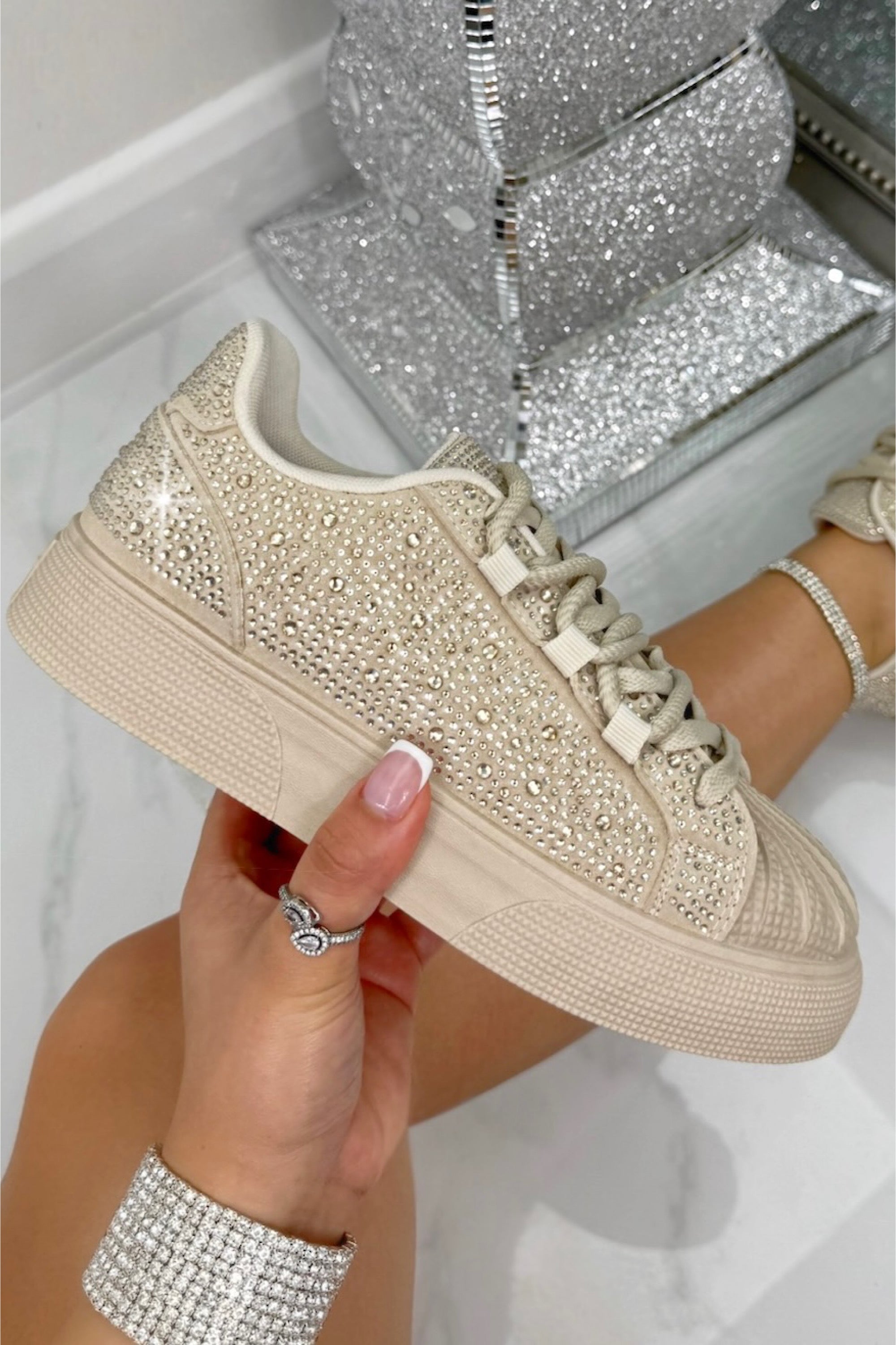Beige sneaker with rhinestone embellishments held by a hand, with a glittery box in the background.