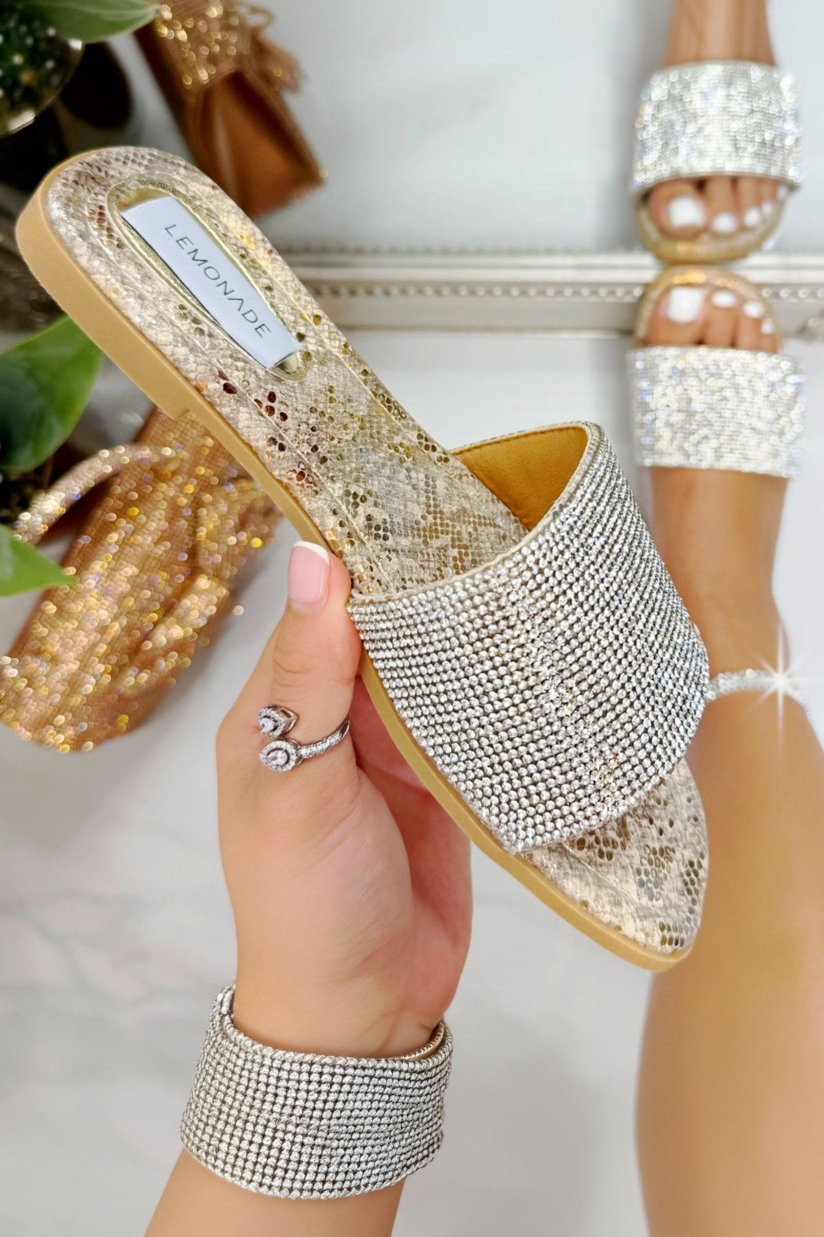 Gold glittery sandal held by a hand with a blurred background