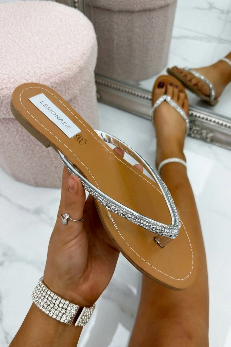 Person holding a tan sandal with rhinestone details, wearing a ring and bracelet, on a light background.