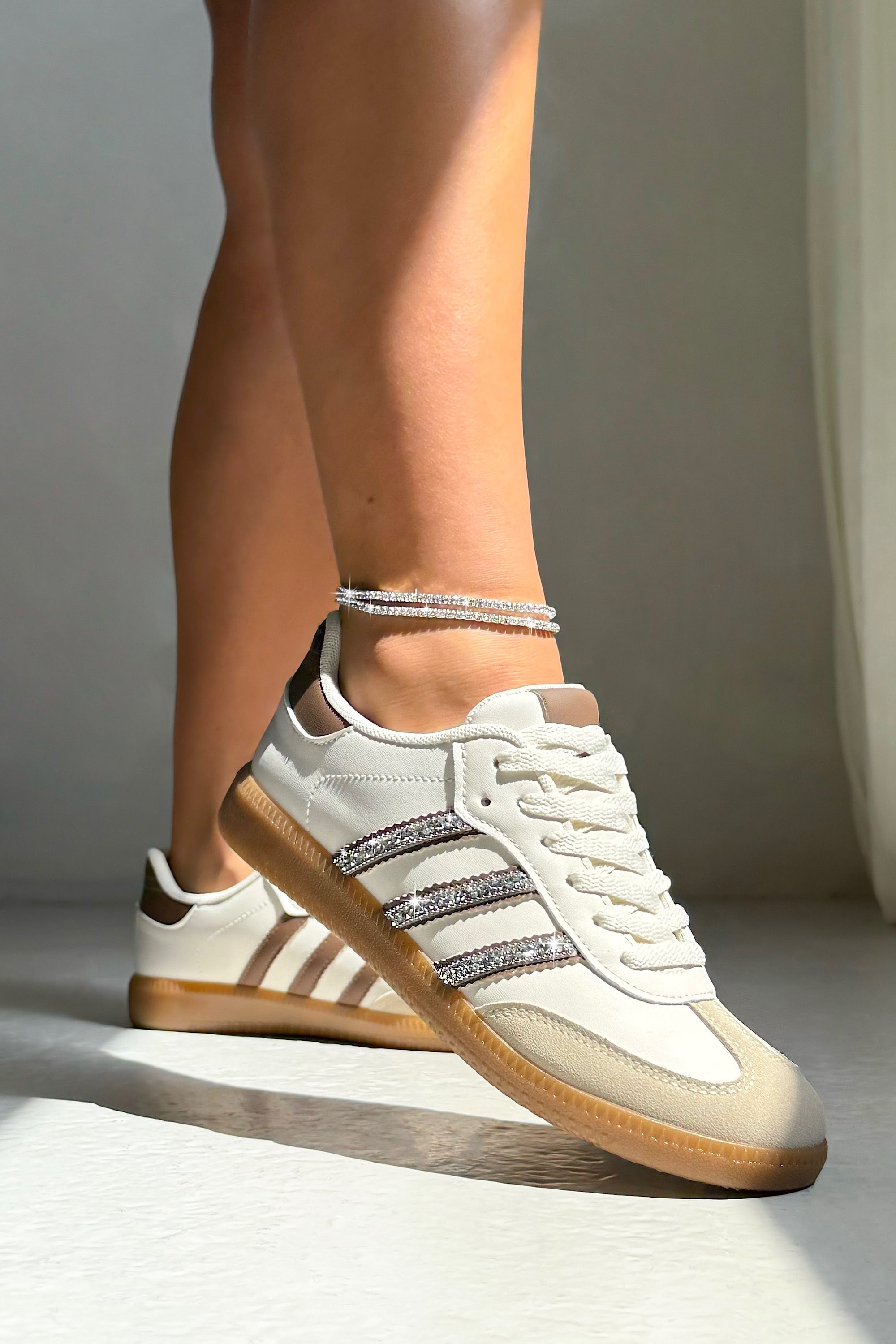 White sneakers with brown soles and stripes worn by a person on a neutral background