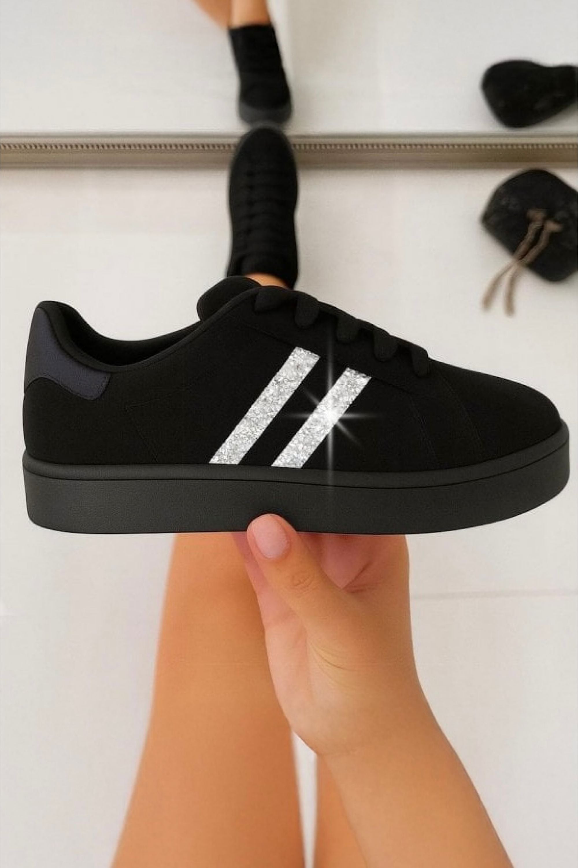 Black sneaker with silver stripes held by a hand against a white background