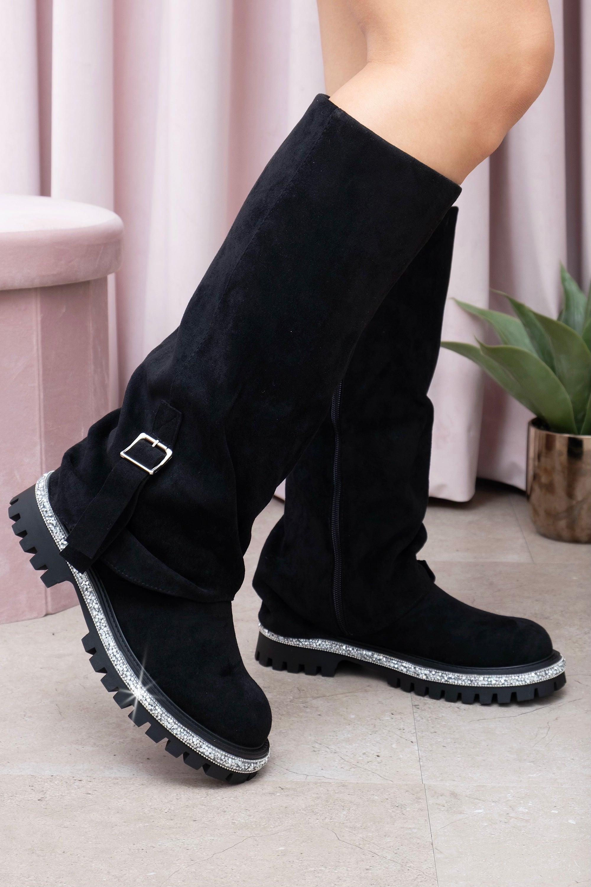 Black knee-high boots with silver buckles worn by a person indoors.
