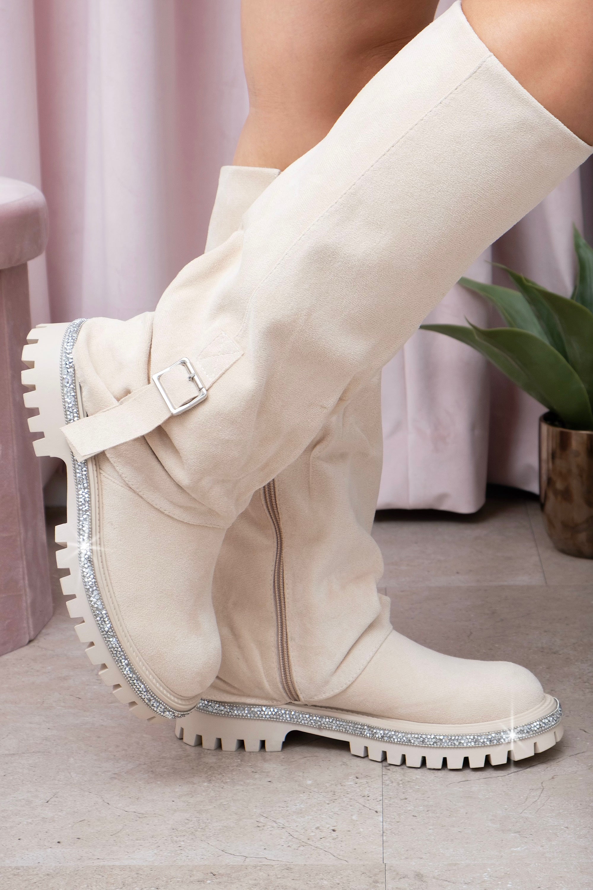 Nude knee-high boots with a textured sole on a light wooden floor.