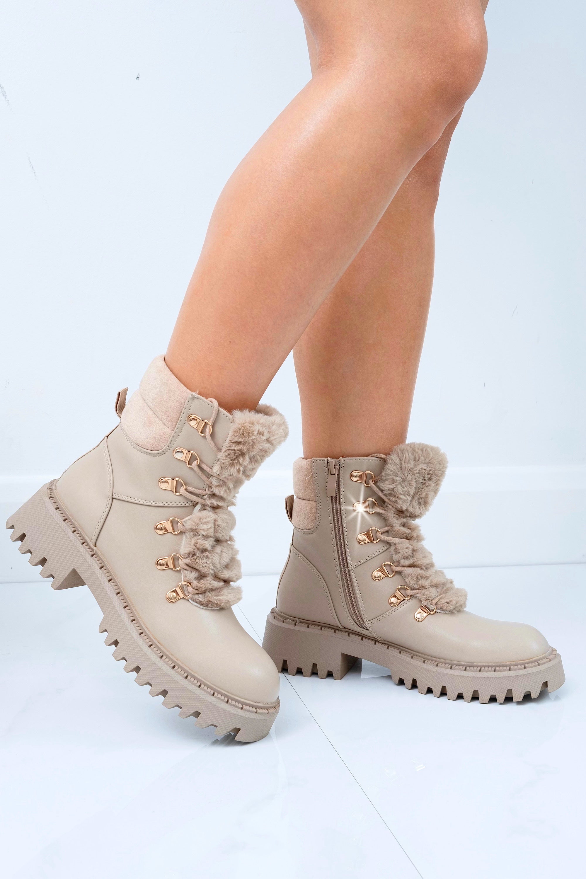 Beige winter boots with gold accents worn by a person on a light blue background