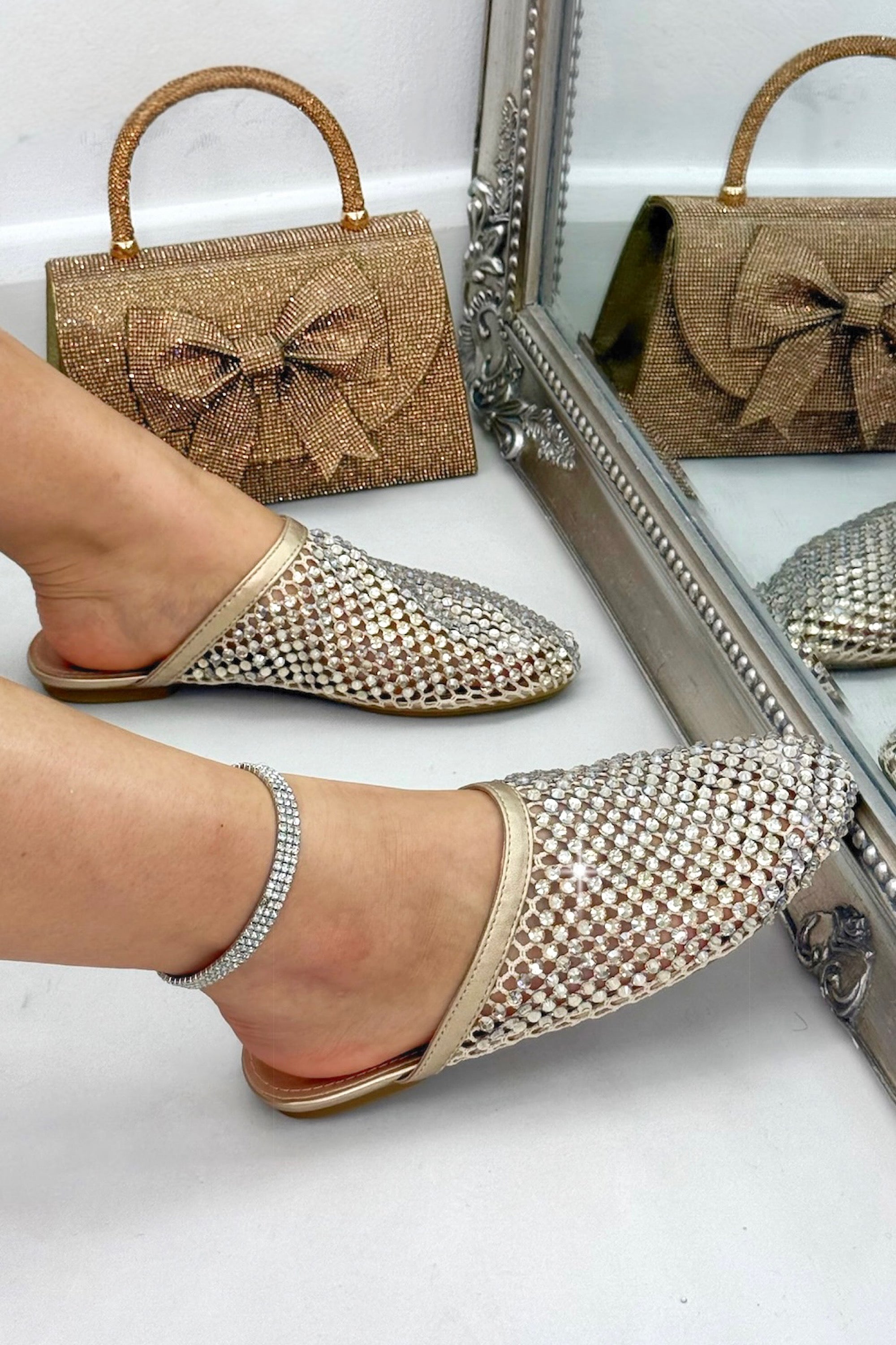 Gold embellished shoes and matching handbag with a bow on a white background