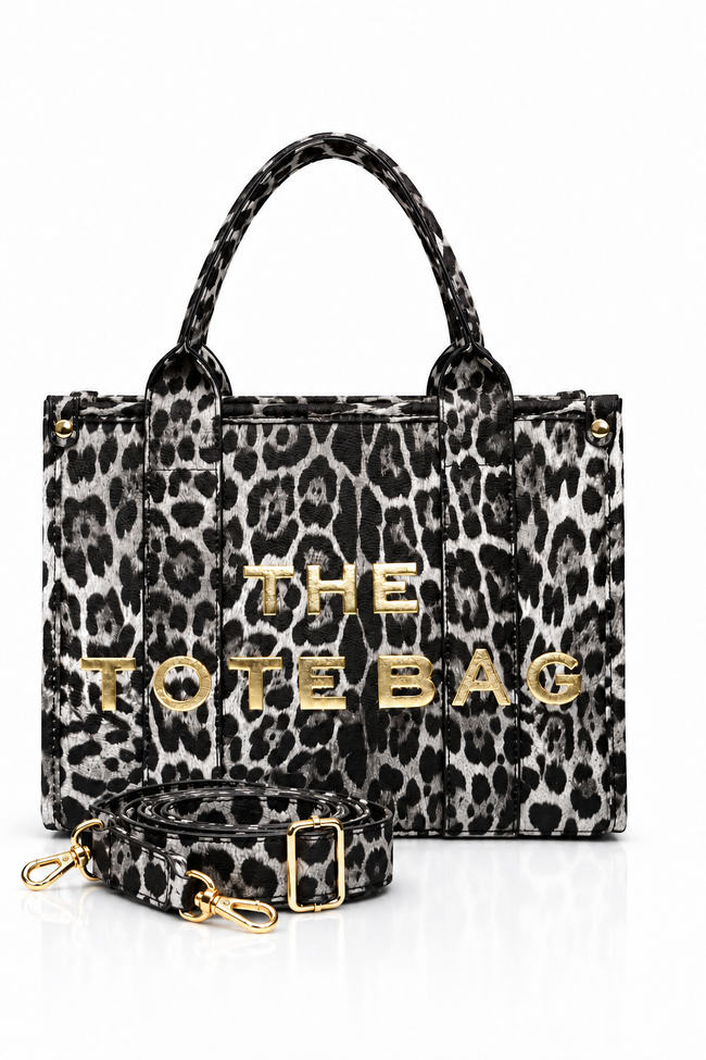 Grey and black Leopard-print tote bag with animal print, two matching top handles, structured rectangular shape and bold gold-tone. "THE TOTE BAG" lettering on the front. Handle of bag pictured in front of bag. Set against a white background.