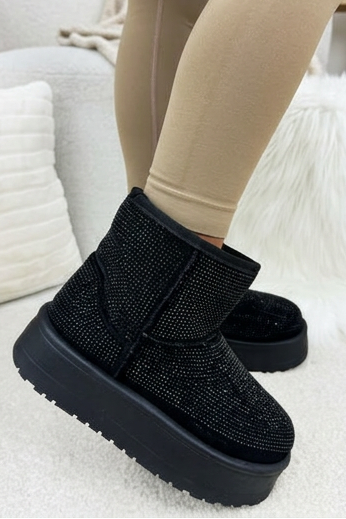 Black textured boots worn with beige leggings on a light-colored surface.