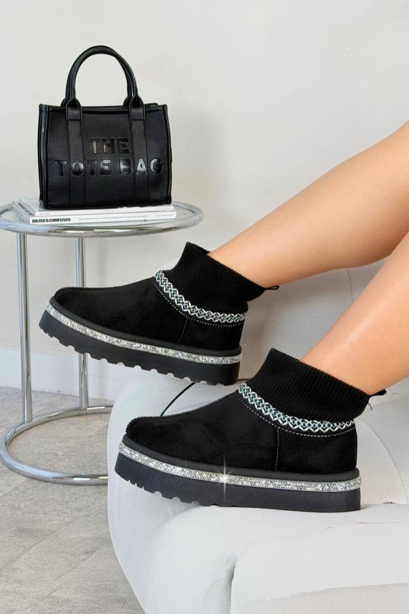Black platform shoes with silver accents worn by a person, with a black handbag in the background.