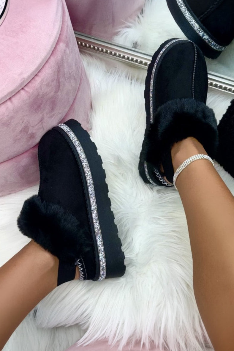Person wearing black fur-lined shoes on a white surface