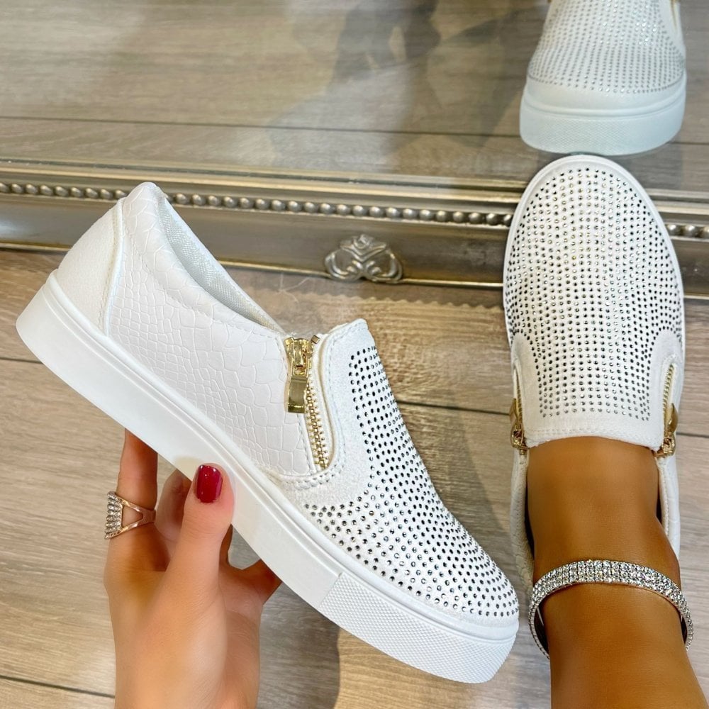 White slip-on sneakers with rhinestone embellishments on a wooden floor.