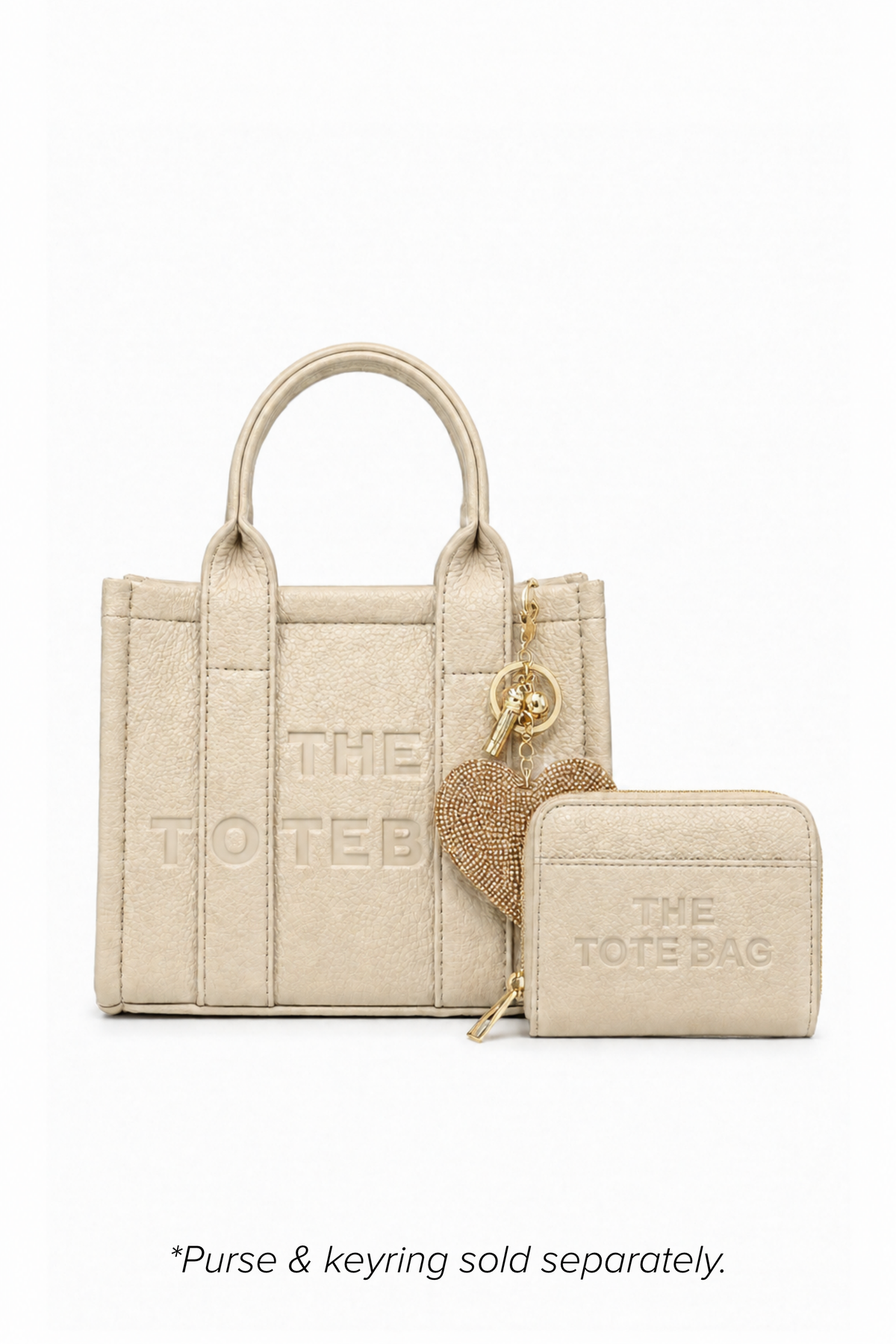Beige mini structured tote bag with two rounded top handles, vertical stitched panels, matching tonal stitching and subtle embossed "THE TOTE BAG" lettering on the front. Shown with matching decorative key ring and rectangular zip purse. Purse and keyring sold separately.  