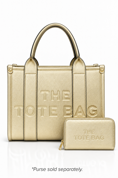 Metallic Gold structured tote bag with two rounded top handles, embossed. "THE TOTE BAG" lettering on the front, vertical stitched panels, contrast edging and gold- tone stud details.  Metallic gold Tote purse pictured in front. Set against a white background.