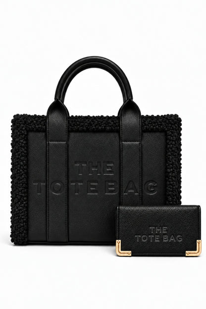 Black tote bag bundle featuring a structured handbag with rounded top handles, textured trim, embossed "THE TOTE BAG" lettering, and matching black straps. Includes a matching black purse with embossed branding and gold-tone corner detailing.