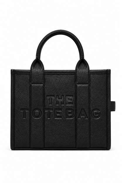 Black faux leather tote bag with two rounded top handles, embossed "THE TOTE BAG" lettering on the front, contrast stitching, gold tone hardware. Set against a white background.