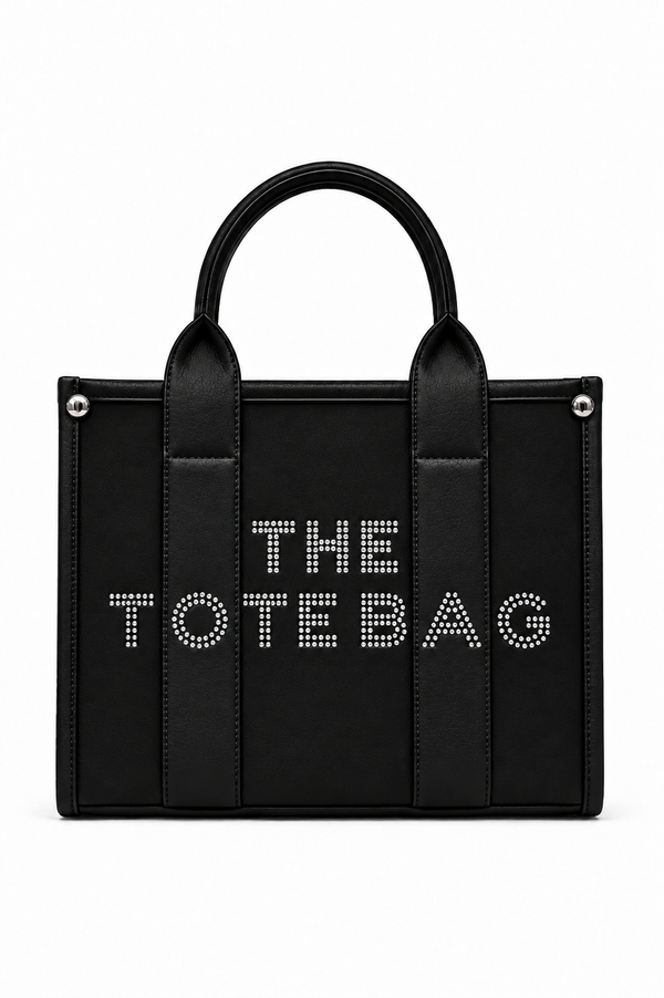 Black structured Tote handbag with two rounded top handles, vertical stitched pictures and silver-tone stud details at the upper corners. Features white studded "THE TOTE BAG" lettering across the front, a top zip.