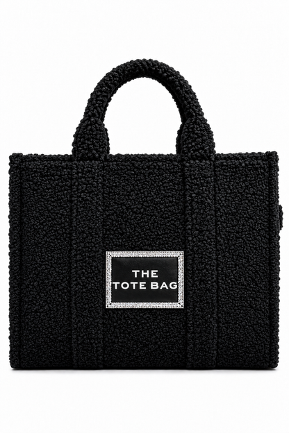 A black textured teddy-bundle tote bag with two top handles and a central silver-bordered label that reads &
