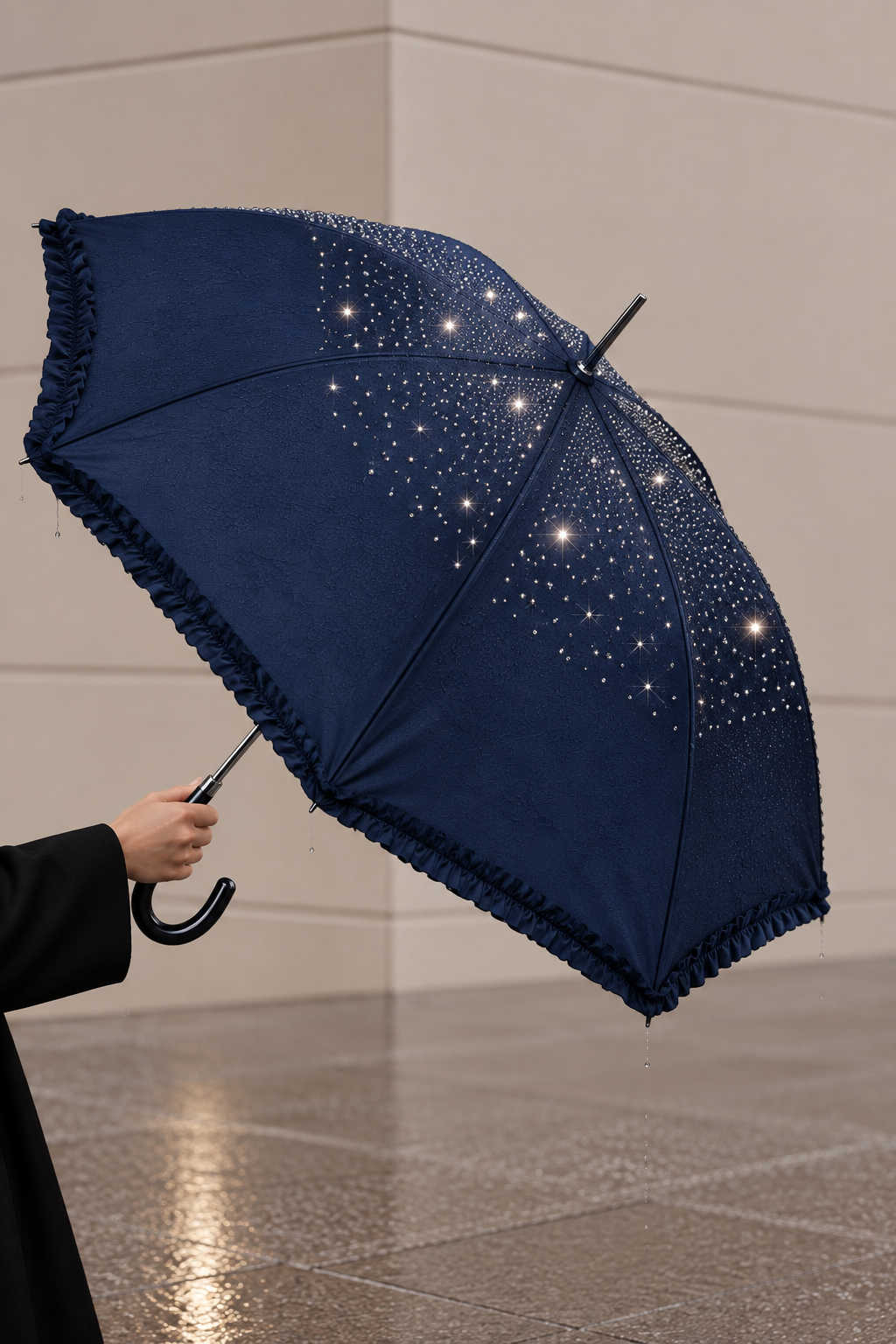 A navy blue umbrella with a ruffled edge and scattered white rhinestone-like embellishments, held open by a person in a black coat in an indoor setting with a tiled floor.