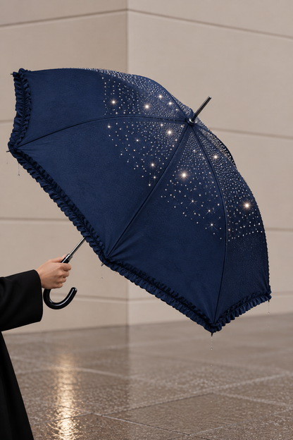 A navy blue umbrella with a ruffled edge and scattered white rhinestone-like embellishments, held open by a person in a black coat in an indoor setting with a tiled floor.
