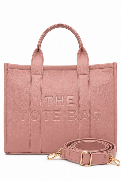 Large Pink faux leather structured tote bag with two rounded top handles, embossed. "THE TOTE BAG" lettering on the front, vertical stitched panels. Pictured on a white background.  With pink-tone strap pictured in front of the bag.