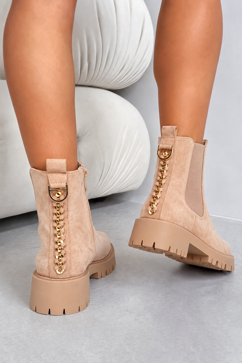 Beige suede ankle boots with gold chain and D-ring hardware, shown on a model&