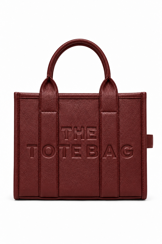 Burgundy Faux leather tote bag with two rounded top handles, embossed "THE TOTE BAG" lettering on the front, contrast stitching. gold tone hardware. Set against a white background.