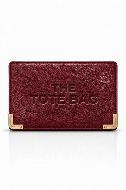 A burgundy textured leather tote bag with gold-tone metal corner brackets and embossed text reading &
