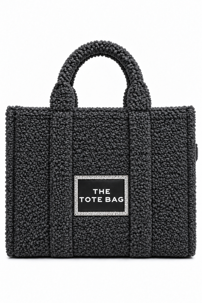 A black bouclé tote bag with dual top handles and a central black label outlined in rhinestones that reads &