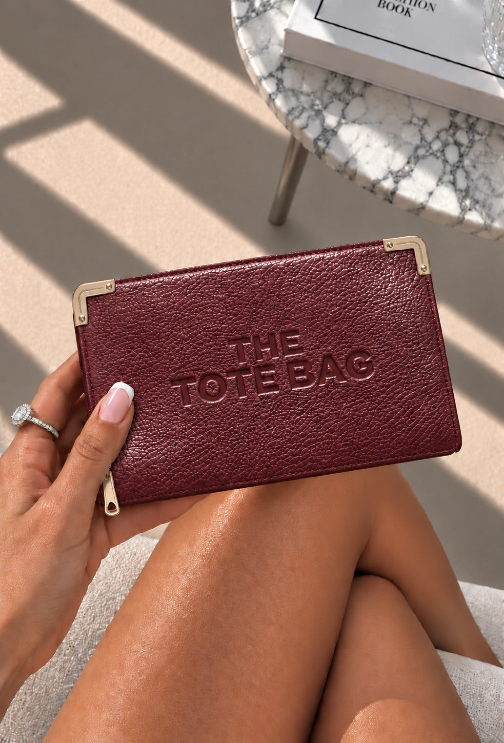 A maroon textured leather tote bag with gold-tone metal corner protectors and embossed &