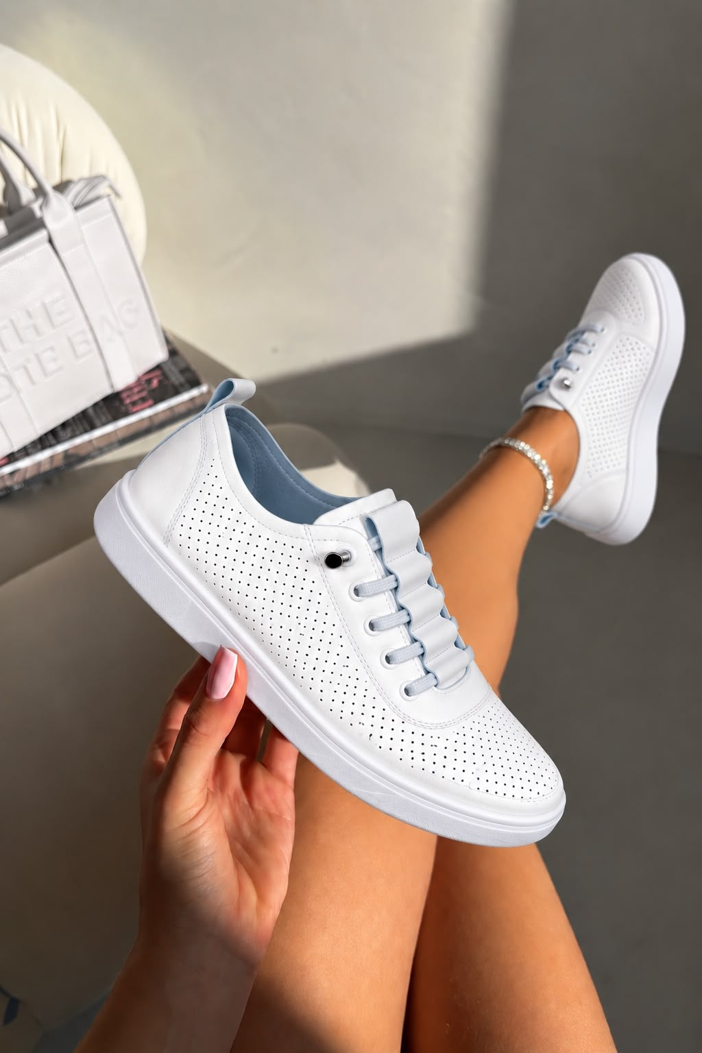 White perforated low-top sneakers with light blue laces, held by a hand and worn on a person&