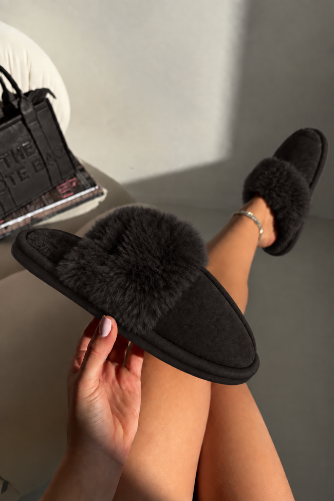 Black fluffy slippers held against a minimalist modern background