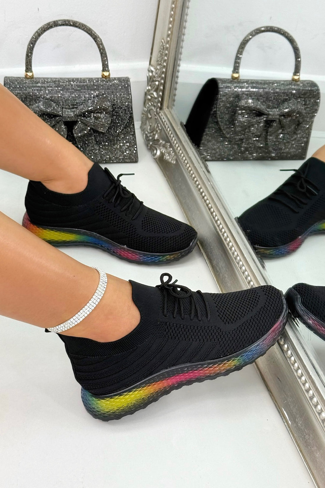 Black sneakers with colorful soles worn by a person, reflected in a mirror.