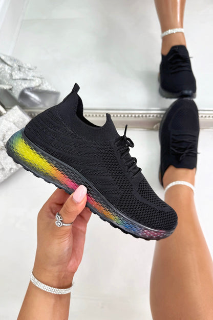 Black sneaker with rainbow sole held by a hand against a white background
