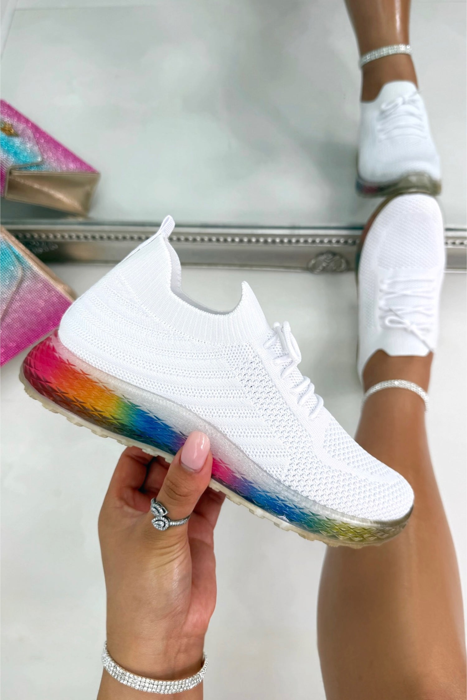 White sneaker with rainbow sole held by a hand, against a blurred background