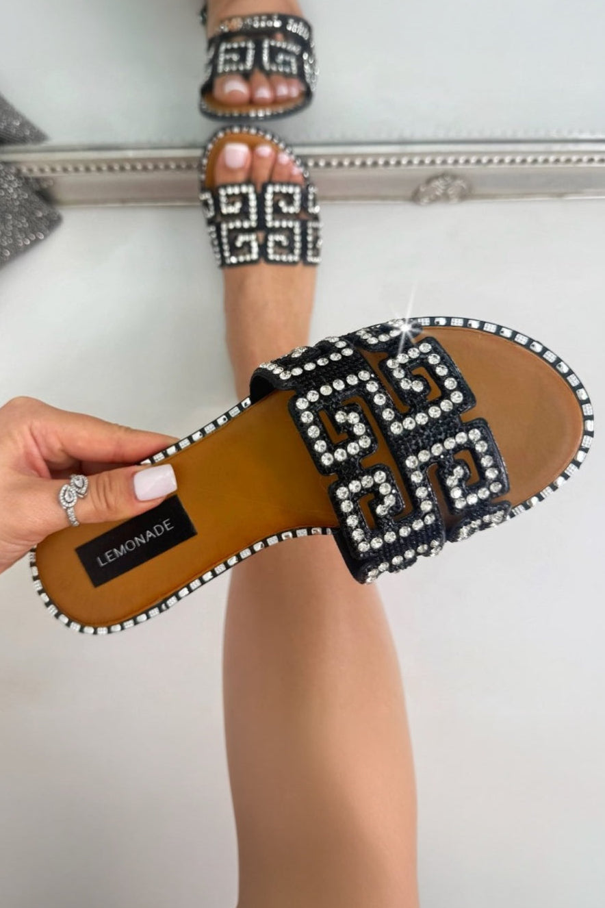 Person holding a sandal with decorative straps and a mirror reflection showing more sandals.