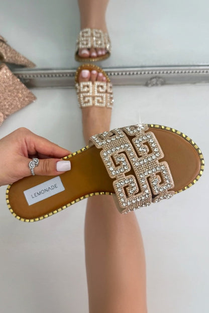 Hand holding a sandal with decorative straps in front of a mirror reflecting high heels.
