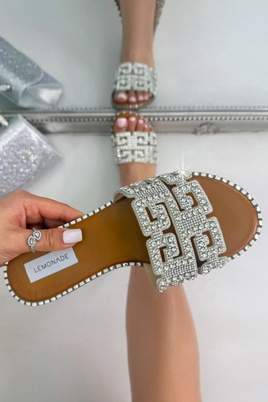 Shiny embellished sandals with a hand holding one, on a light background