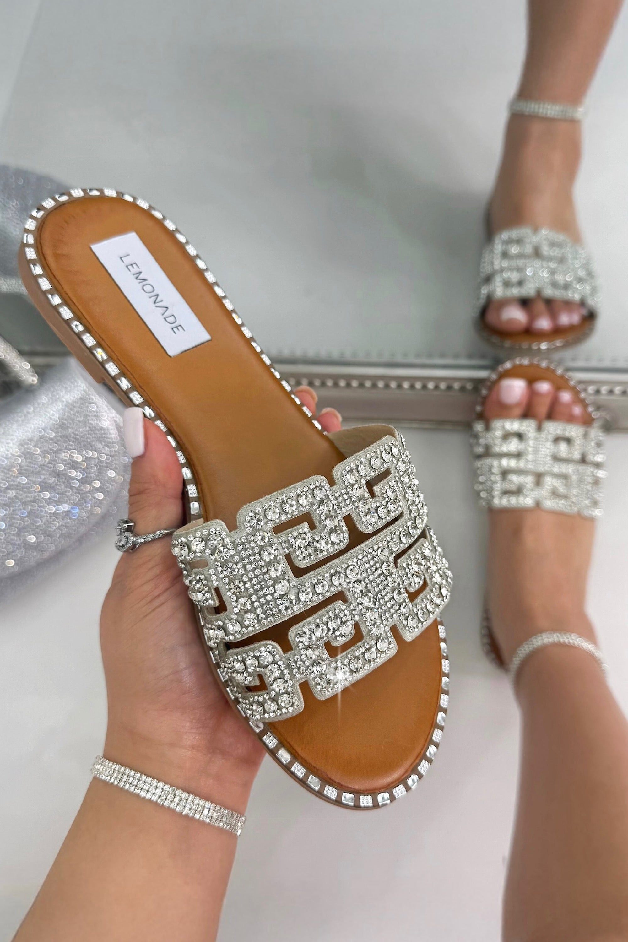 Bridal sandal with rhinestone embellishments held by a hand, with another sandal on foot in the background.