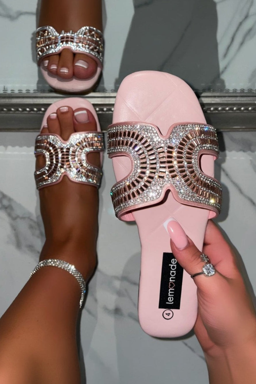 Pink slide sandals with embellishments held by a hand against a marble background