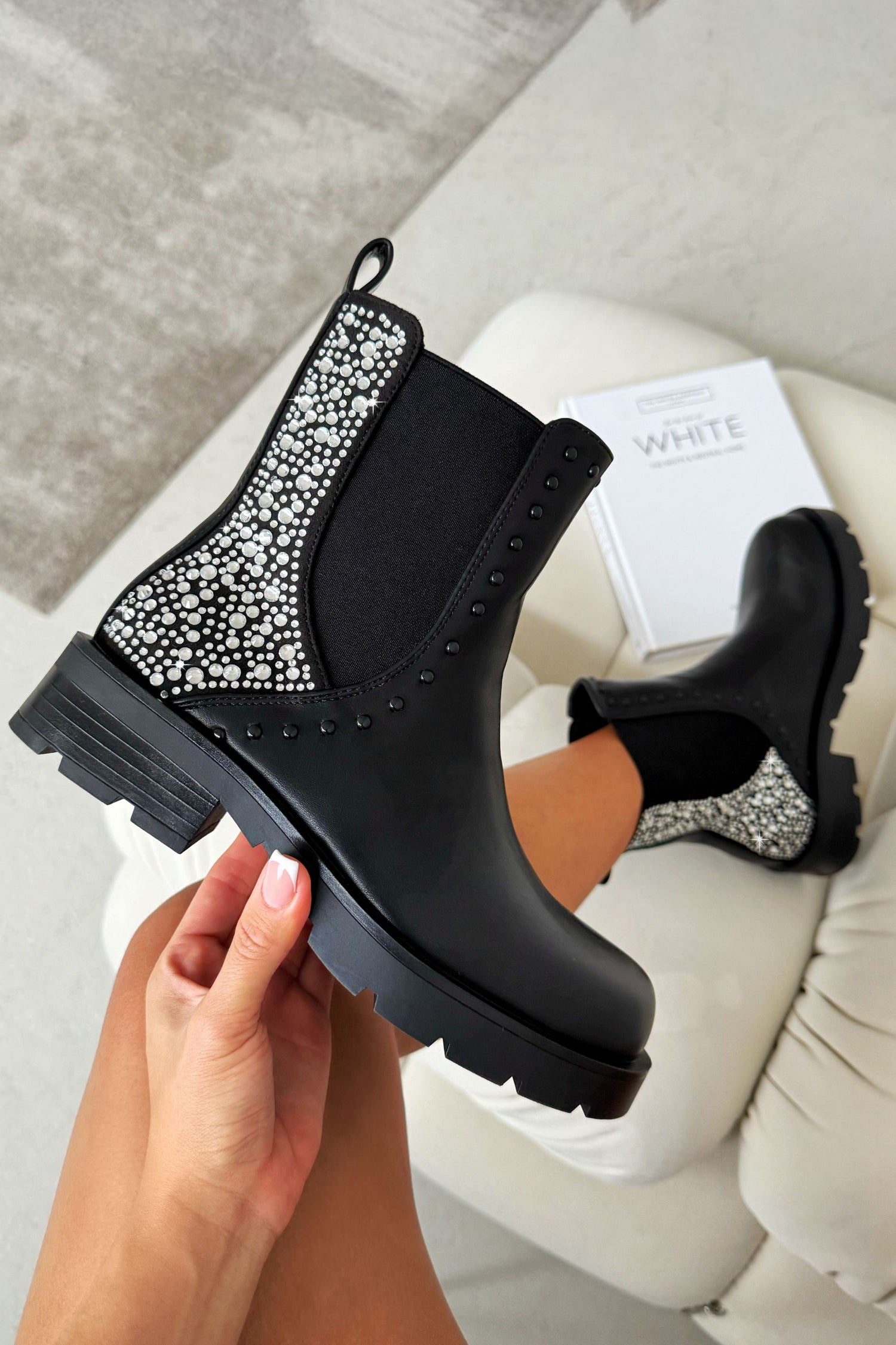 Black Chelsea boots with rhinestone details held by a hand on a light background