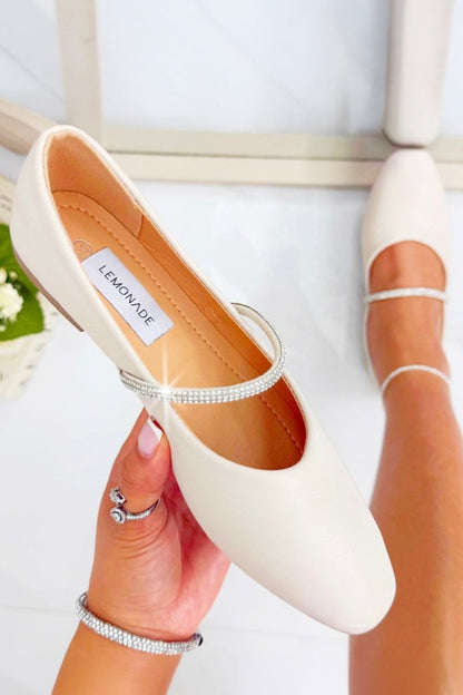 White ballet flats held by a hand with a ring, on a light background
