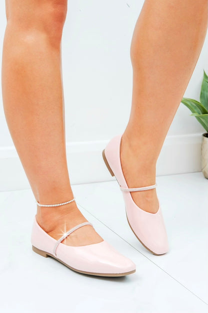 Pink flat shoes worn by a person on a white floor with a plant in the background