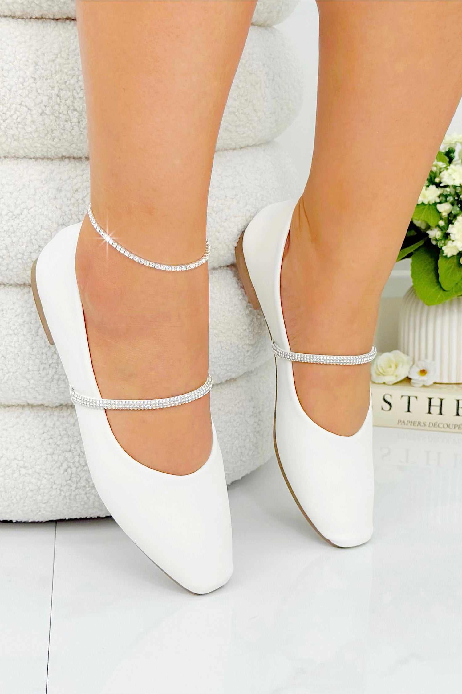 White ballerina shoes with ankle straps worn by a person on a light background