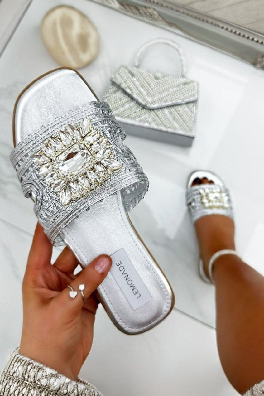 Silver embellished sandals being worn with a matching clutch on a light background