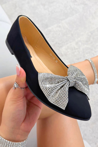 Black flat shoe with a large crystal bow held by a hand against a light background