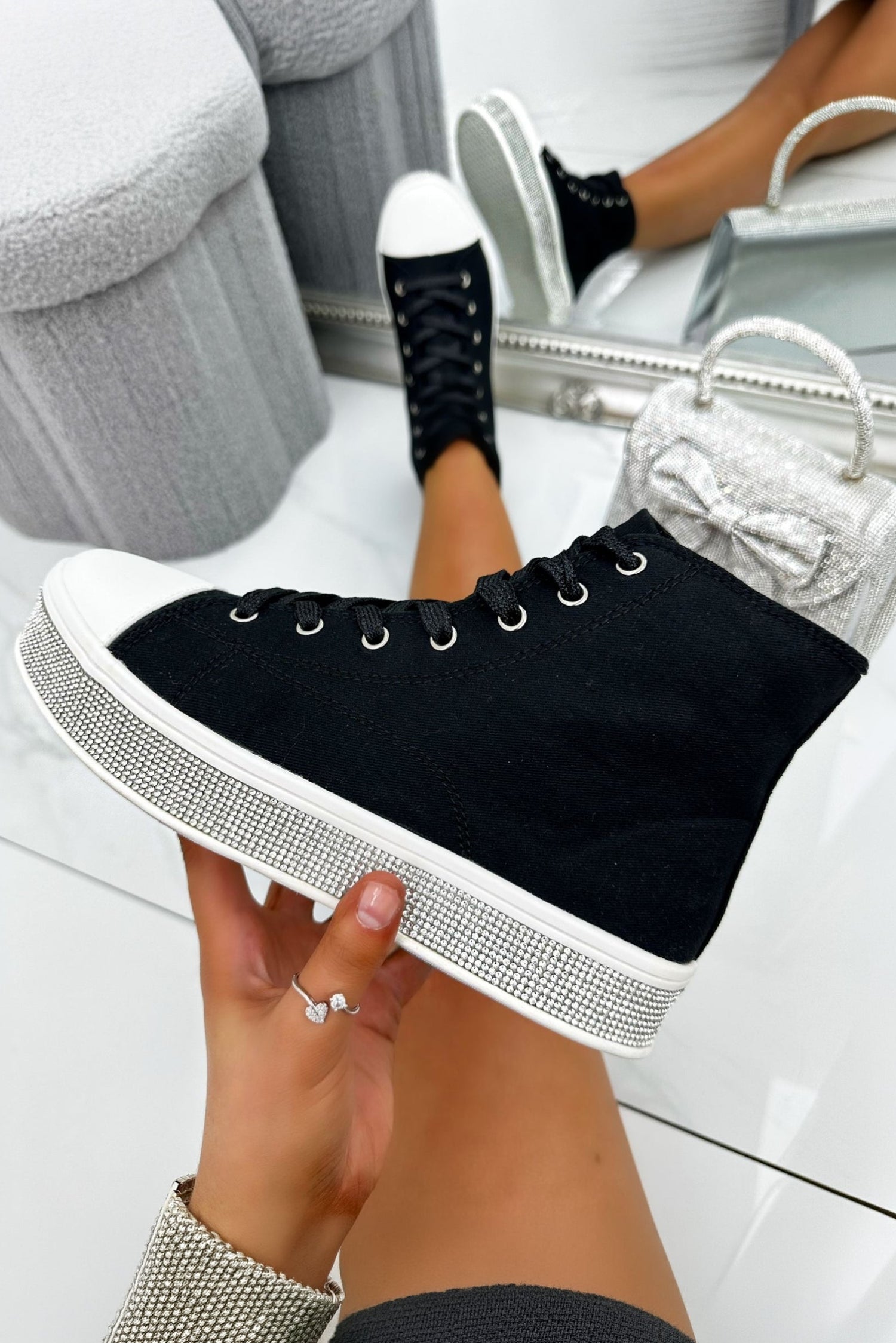 Black high-top sneakers with white soles held by a hand on a light background