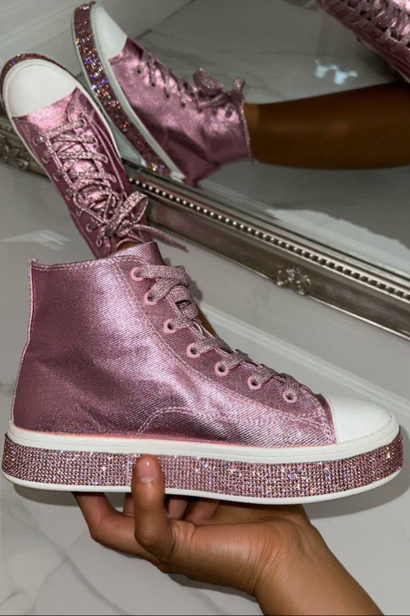 Pink glittery high-top sneakers with white soles held by a hand in front of a mirror.