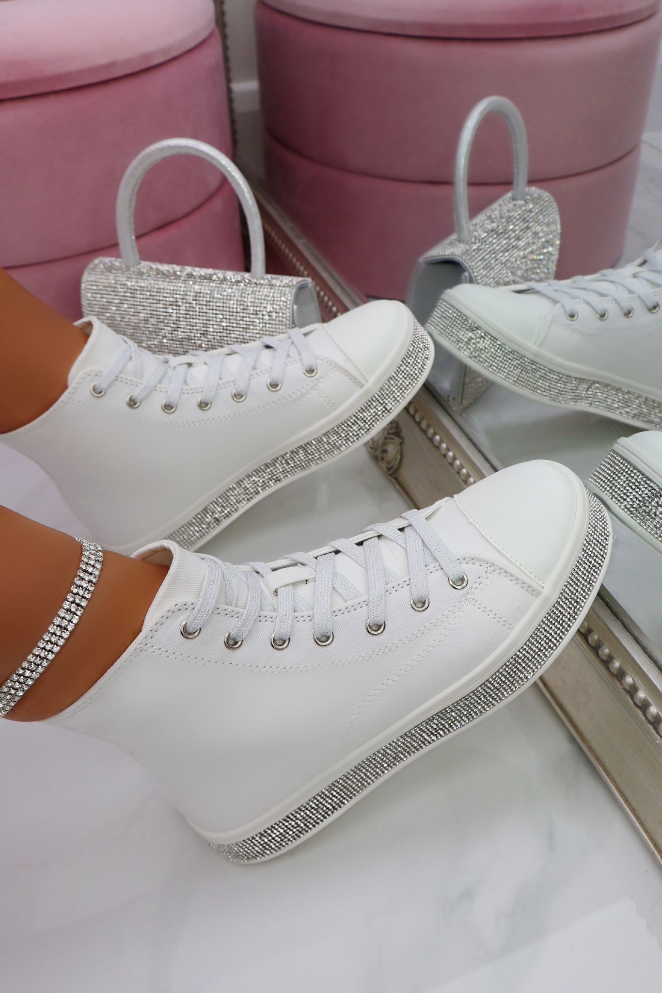 White sneakers with rhinestone details on a white surface with pink stools in the background.