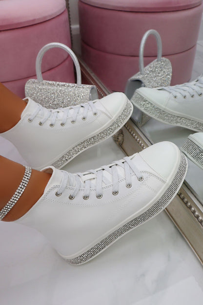 White sneakers with rhinestone details on a white surface with pink stools in the background.